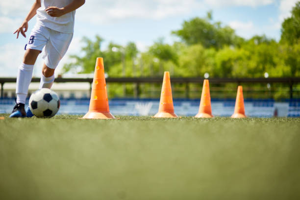 Junger Fußballspieler dribbelt den Ball im Slalom durch Pylonen