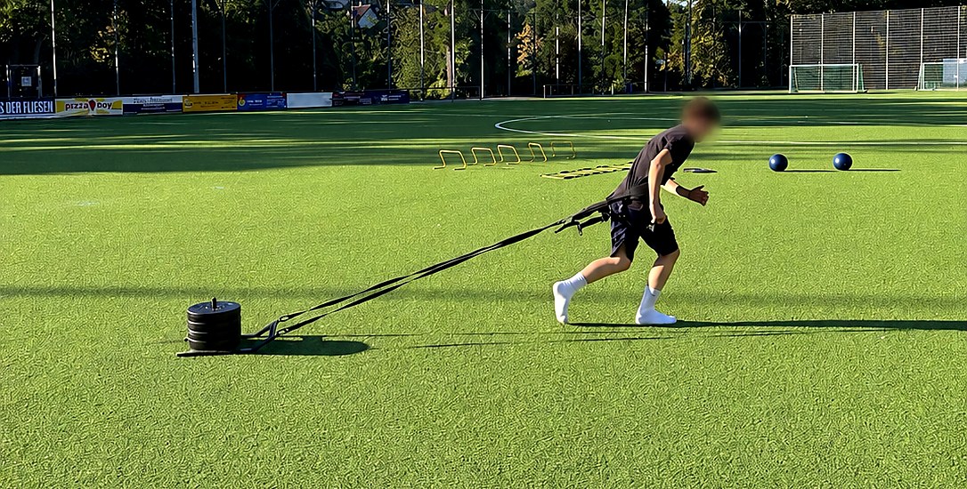 Athletiktraining der Rasenhelden Fußballschule in Wiesbaden — Spieler zieht Gewichtsschlitten auf dem Kunstrasen